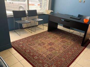 Office space with blue walls, black desk, chairs, and a patterned rug.
