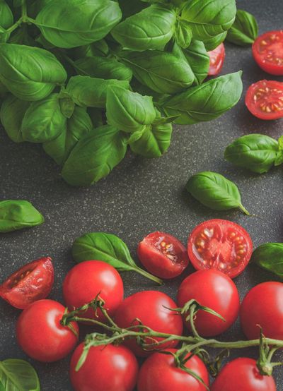 cherry tomatoes on the vine (some sliced) and fresh basil on a cutting board.
