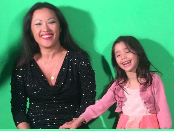 A smiling woman and girl hold hands against a green screen.