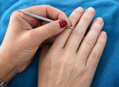 Hand using a metal tool on another hand's finger against a blue background.