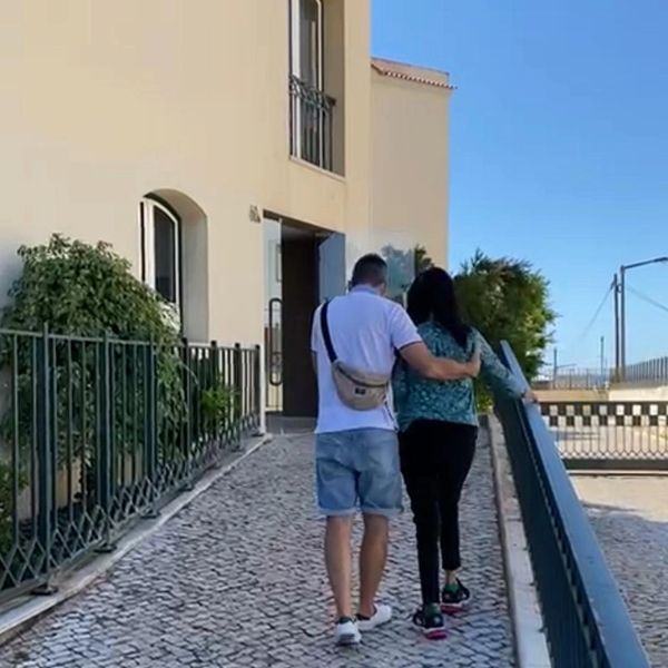 A couple walking arm in arm on a cobblestone path beside a building.