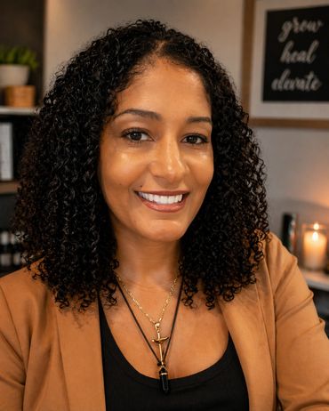 Smiling woman with curly hair wearing layered necklaces and a brown jacket.