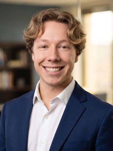Young man in a blue suit smiling warmly for a professional portrait.