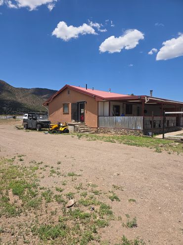 Rural house with parked vehicles and mountainous backdrop.