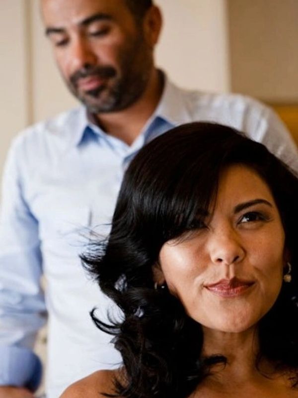 Woman with styled dark hair and a man in the background.