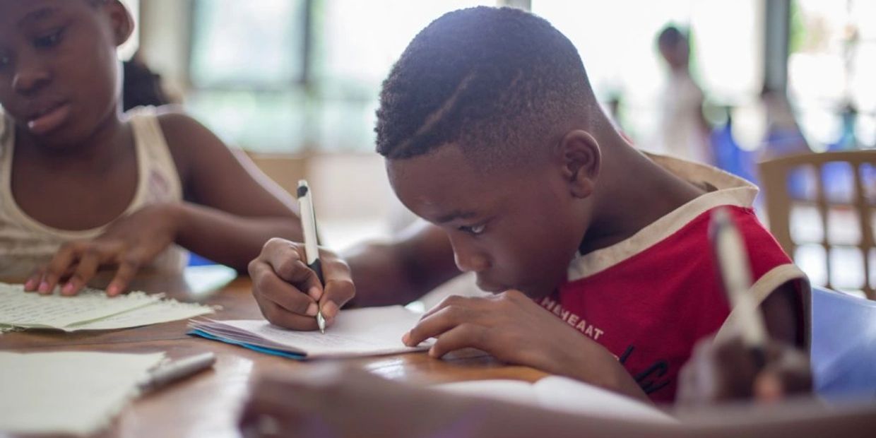 Young boy focused on writing at a classroom desk.