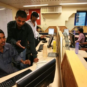 A group of young men working together in a busy office with computers.