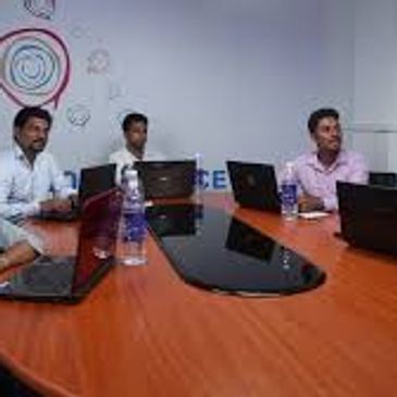 Five people in a meeting room with laptops around a table.
