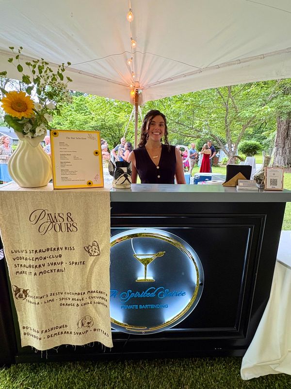 Smiling bartender at an outdoor event under a tent.