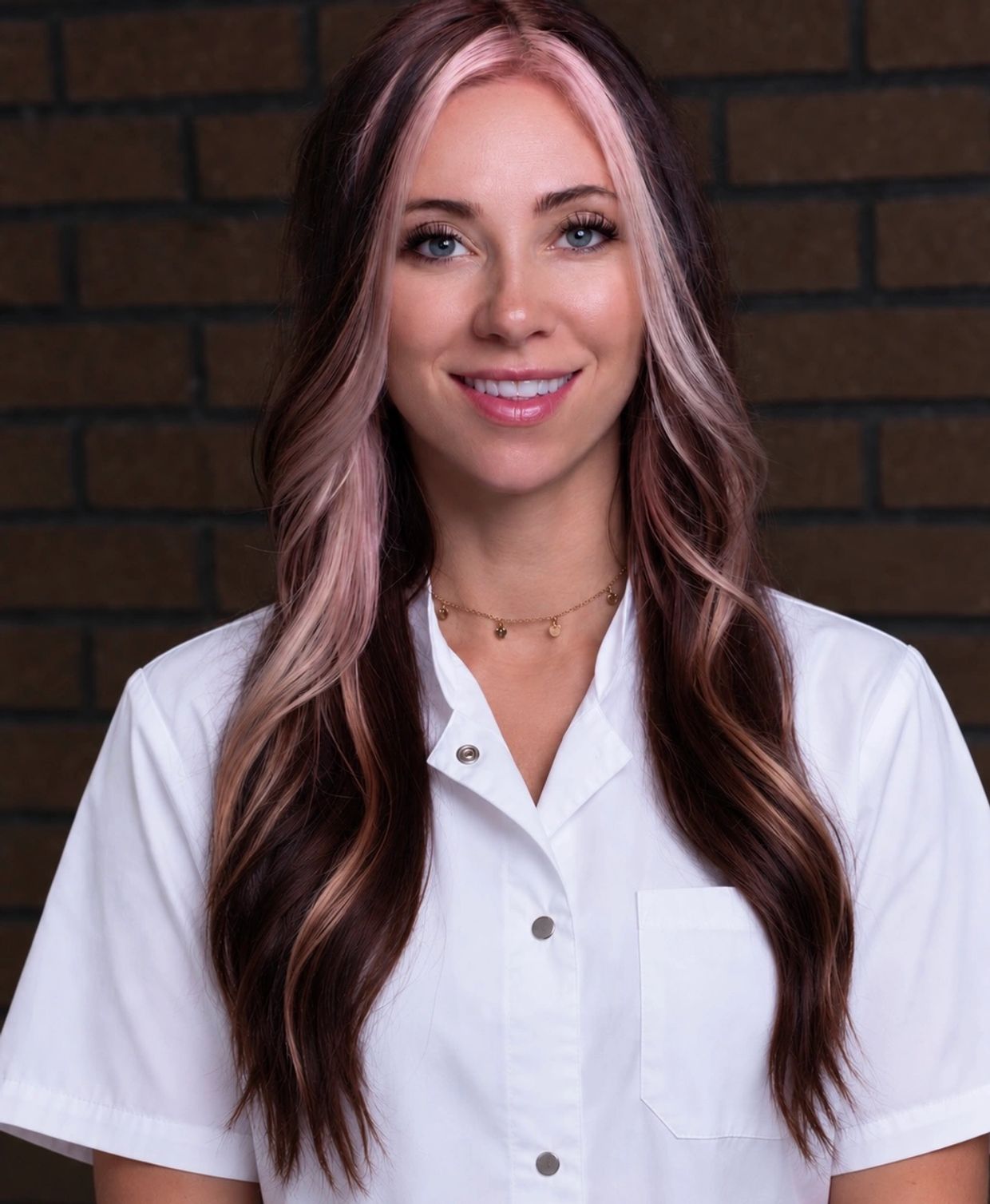 Smiling woman with pink highlights wearing a white coat.