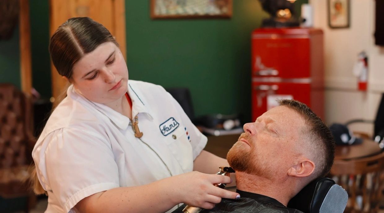 Barber carefully trims a man's beard in a cozy barbershop.