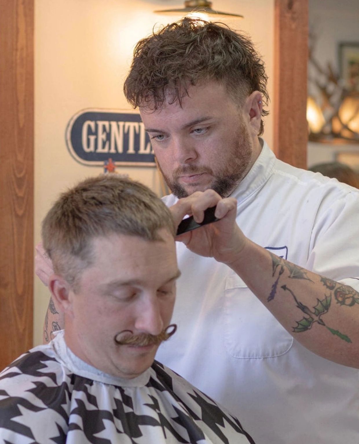 Barber giving a haircut to a man with a handlebar mustache.