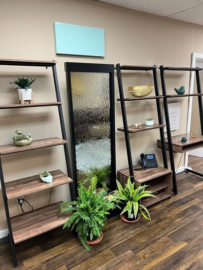 Angled decorative shelves with small plants below a plaque reading "Be Kind"