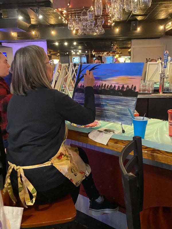 Woman painting a sunset landscape at a bar art class.