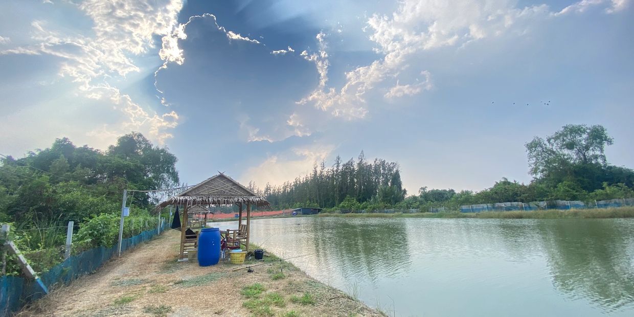 A serene lakeside hut under a dramatic sky with sun rays and trees around.