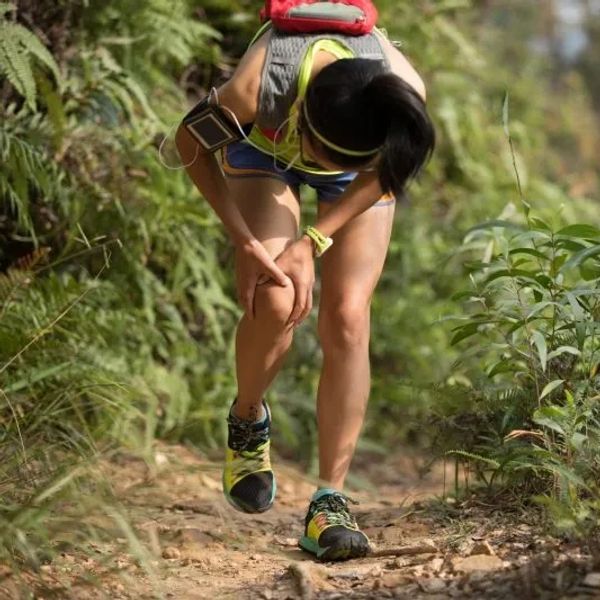 A runner clutching her knee in pain on a forest trail.