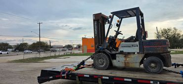 Rusty Komatsu forklift secured on a flatbed trailer at sunset.