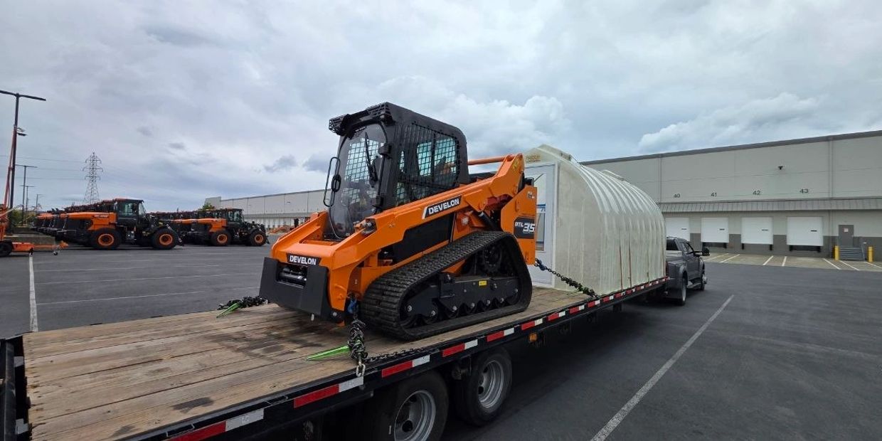Orange Develon compact track loader loaded on a flatbed trailer outdoors.