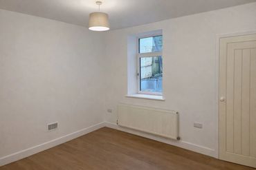 Empty room with white walls, wooden floor, and a small window.