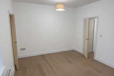 Empty room with white walls, wooden floor, and two doors.