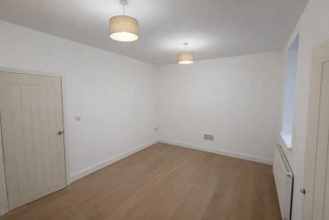 Empty room with white walls, wooden floor, and ceiling lights.