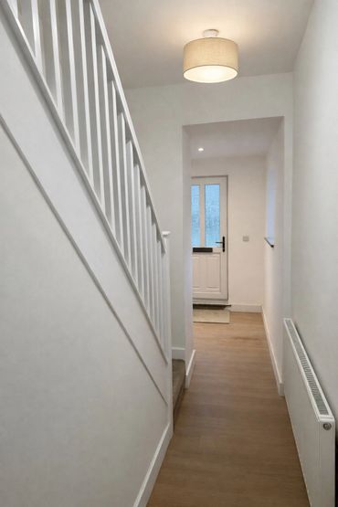 Minimalist hallway with white walls, wooden floor, and staircase.