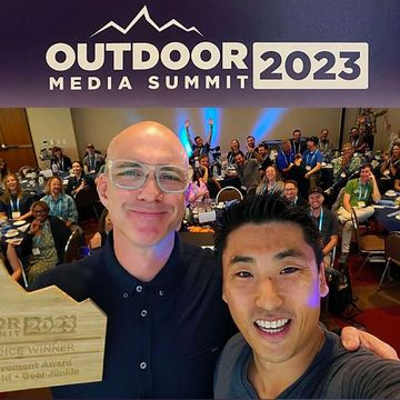 Two men smiling with a group at Outdoor Media Summit 2023.