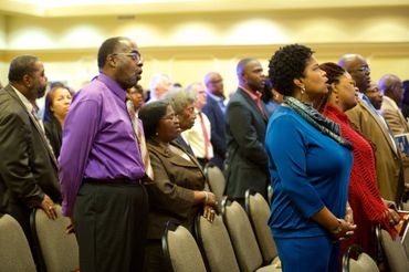 A diverse group of people standing attentively in a conference room.