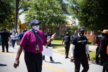 People participating in a peaceful march wearing masks and holding signs.