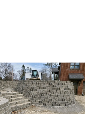 Curved retaining wall and steps made of gray stone blocks near a brick building.