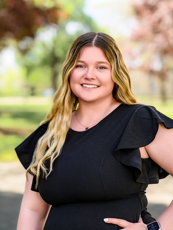 Young woman smiling outdoors in a black dress with ruffled sleeves.