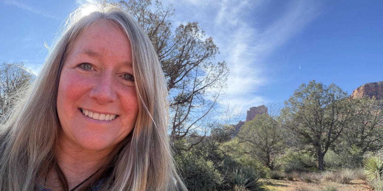 Smiling woman with long blonde hair outdoors on a sunny day.