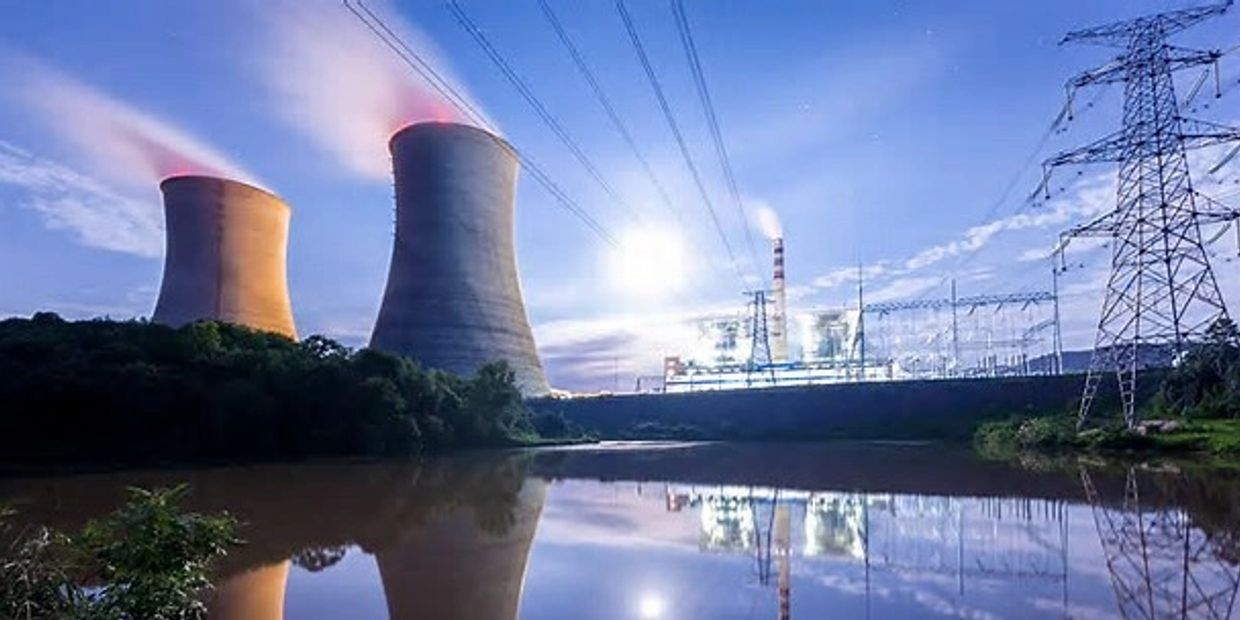 Nuclear power plant with cooling towers and electrical pylons reflected in water.