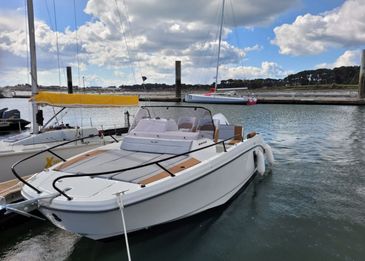 A sleek white motorboat docked at a marina under a partly cloudy sky.