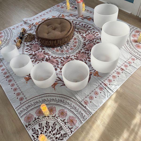 Meditative sound healing setup with crystal bowls, candles, and cushion on a floral mat. Sound Bath Sound Healing Guided Meditation Hypnosis Syracuse CNY
