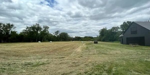 Open field with scattered hay bales under a cloudy sky near a barn.