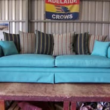 A turquoise sofa with patterned cushions under an Adelaide Crows banner.