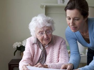 A young woman helps an elderly woman with paperwork at home.