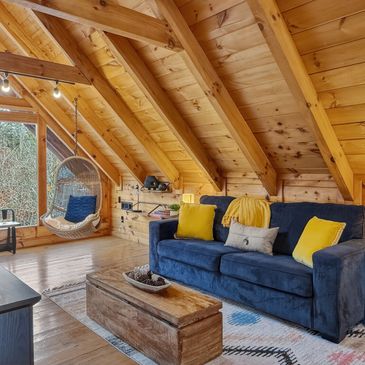 Cozy attic cabin living room with wooden beams and a hanging chair.