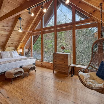 Cozy wooden bedroom with large windows and a hanging chair.