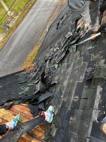 Workers removing old shingles from a roof during roofing repair.