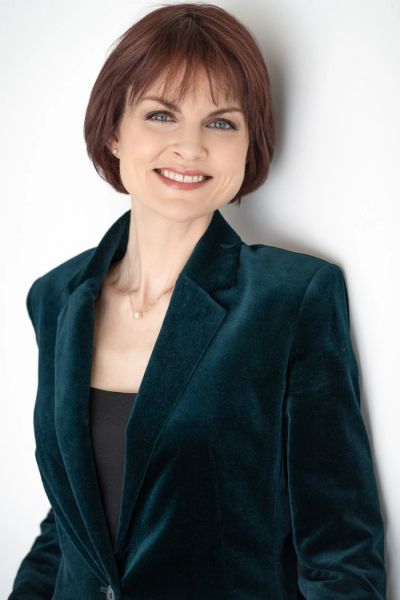 Smiling woman wearing a teal velvet blazer.