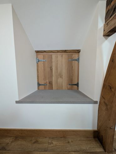 Small wooden door under a sloped ceiling with gray shelf and wooden floor.