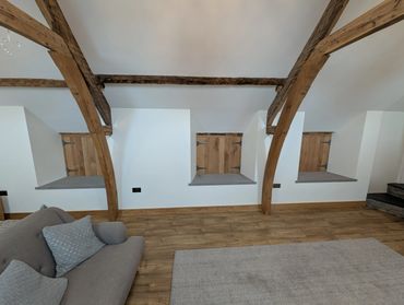Cozy attic space with exposed wooden beams, small wooden doors, and a gray sofa.
