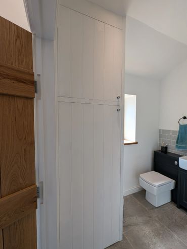 White wooden cabinet with two doors in a modern bathroom corner.