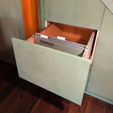 An open green filing cabinet drawer with a hanging folder labeled 'STAPLES'.