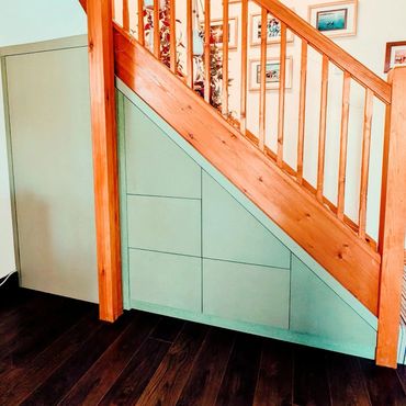 Under-staircase storage cabinets painted green with wooden railing above.
