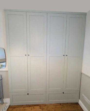 Tall, light gray wardrobe with four paneled doors and two lower drawers in a bedroom.