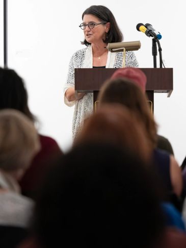 Woman speaking at a podium with audience in front.