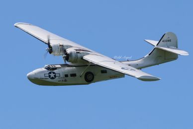 Vintage military seaplane flying against a clear blue sky.